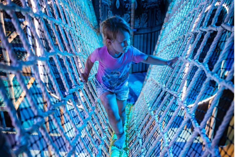 Kind loopt over een verlicht klimnet in de indoor speeltuin Atlantis